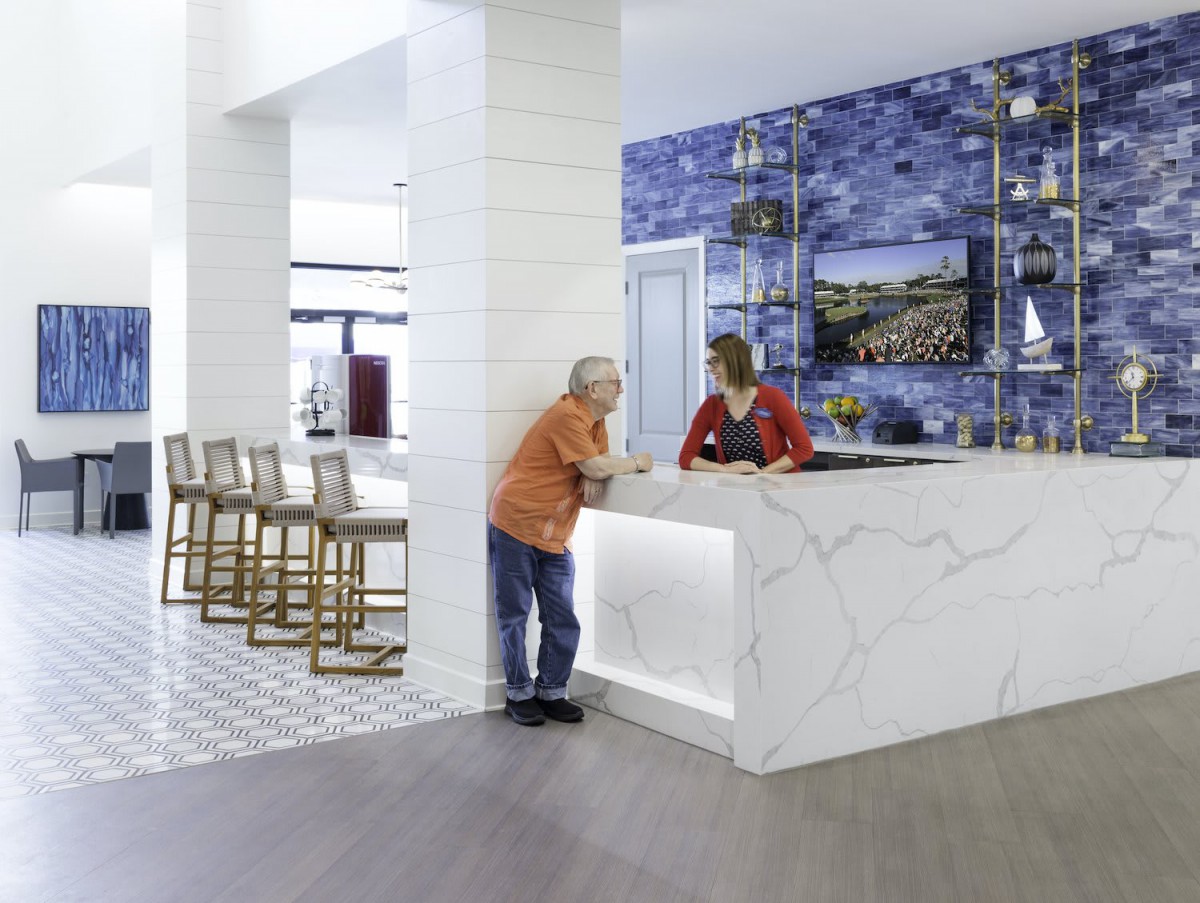A modern hotel lobby with a reception counter where two people are conversing.