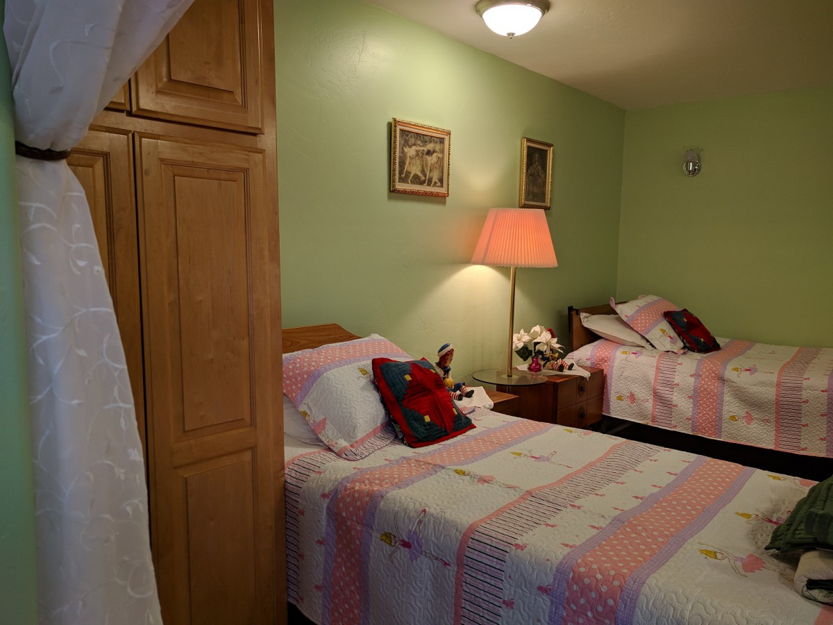 A cozy bedroom featuring twin beds with pink and white bedding, a nightstand with a lamp, and wooden furniture.