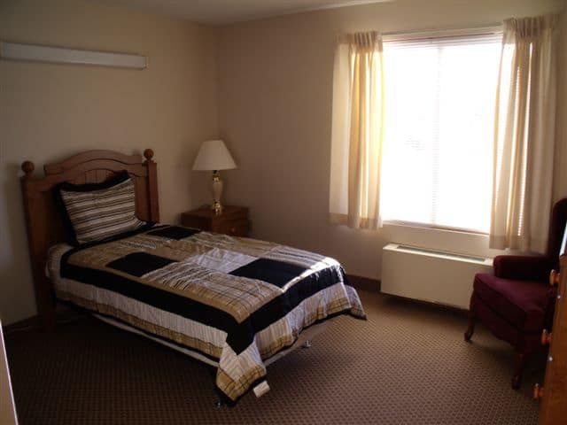 A cozy bedroom with a single bed, bedside lamp, and window with curtains.