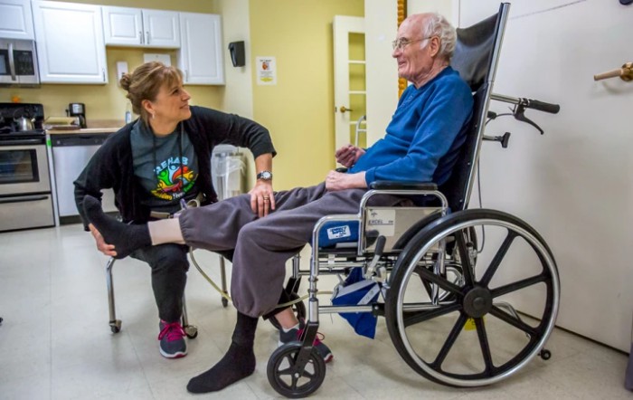 A caregiver interacting with an elderly person in a wheelchair at a healthcare facility.