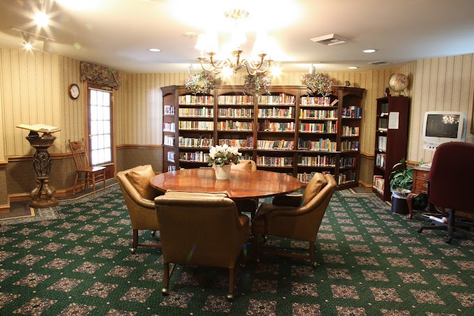 A cozy library room with a round table surrounded by chairs and bookshelves filled with books.
