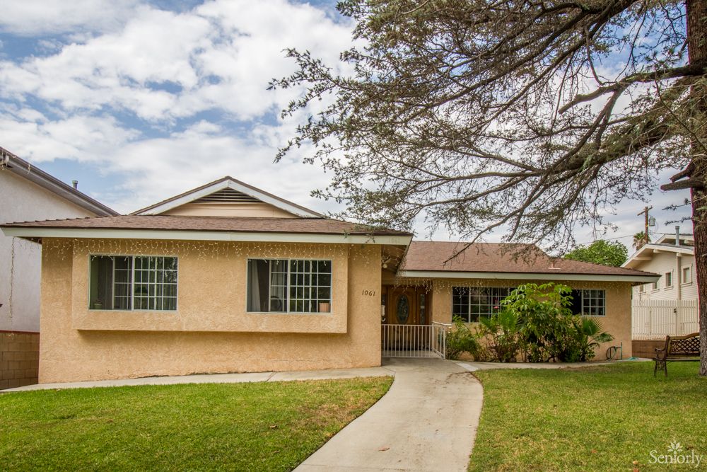 A suburban house with a front lawn and a tree, featuring a concrete pathway leading to the entrance.