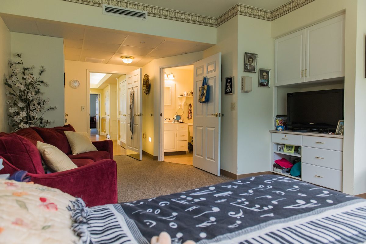 A cozy bedroom with a bed, TV, and seating area leading to a lit bathroom.