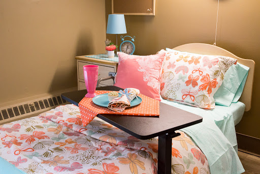 A cozy bedroom setup featuring a floral bedding, a bedside table with a lamp, and a snack tray.