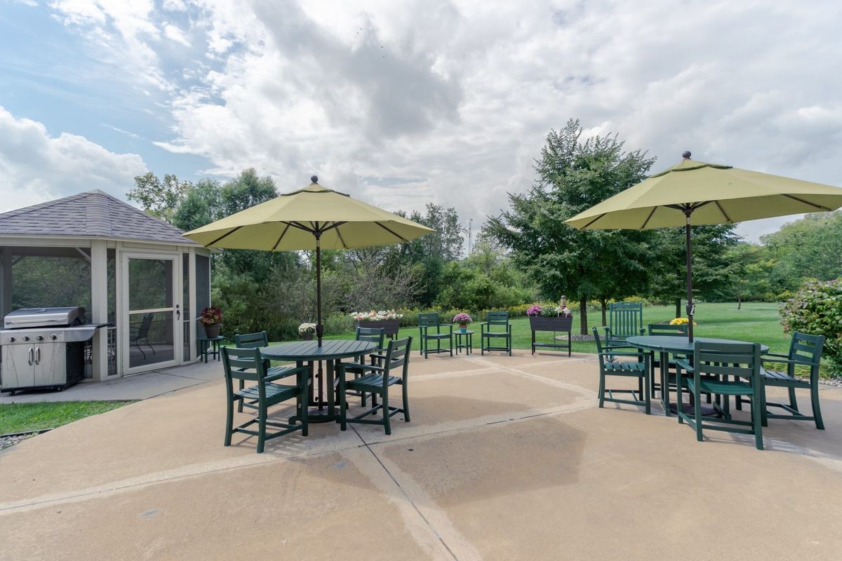 A serene outdoor patio area with tables, chairs, and umbrellas surrounded by greenery.