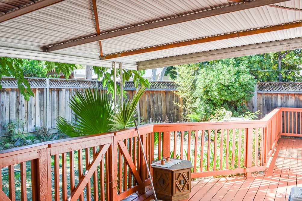 A wooden deck with a covered roof overlooking a garden with lush greenery.