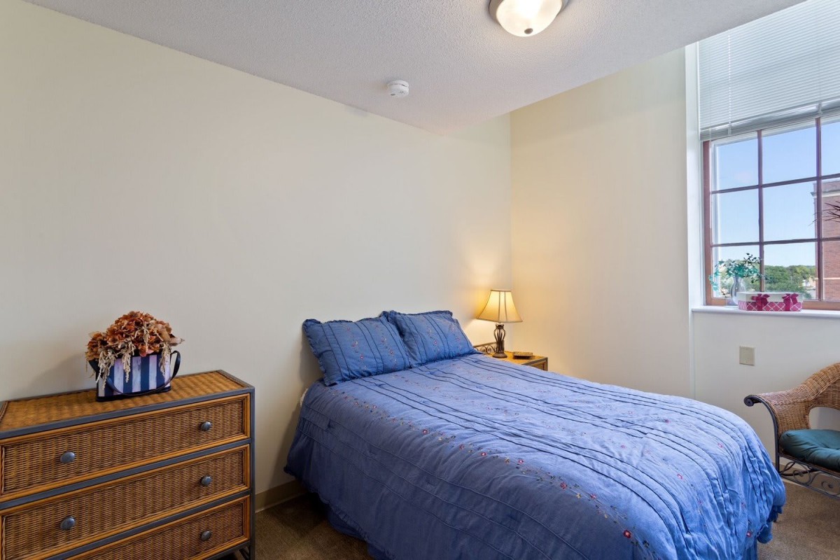 A simple bedroom with a blue bedspread and a wooden dresser.