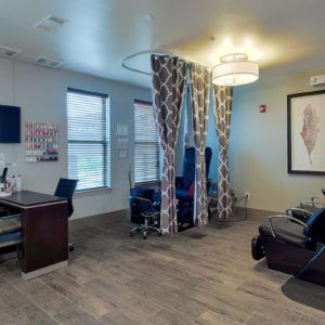 A clinic treatment room with chairs, a desk, and partition curtains.