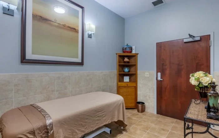 A serene spa room with a massage table, wooden cabinet, and calming decor.