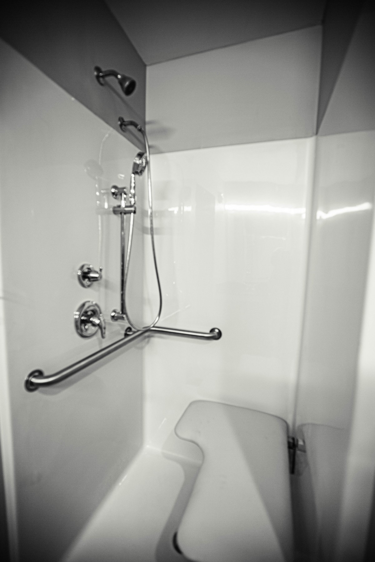 A modern, accessible shower with a grab bar in a white bathroom.