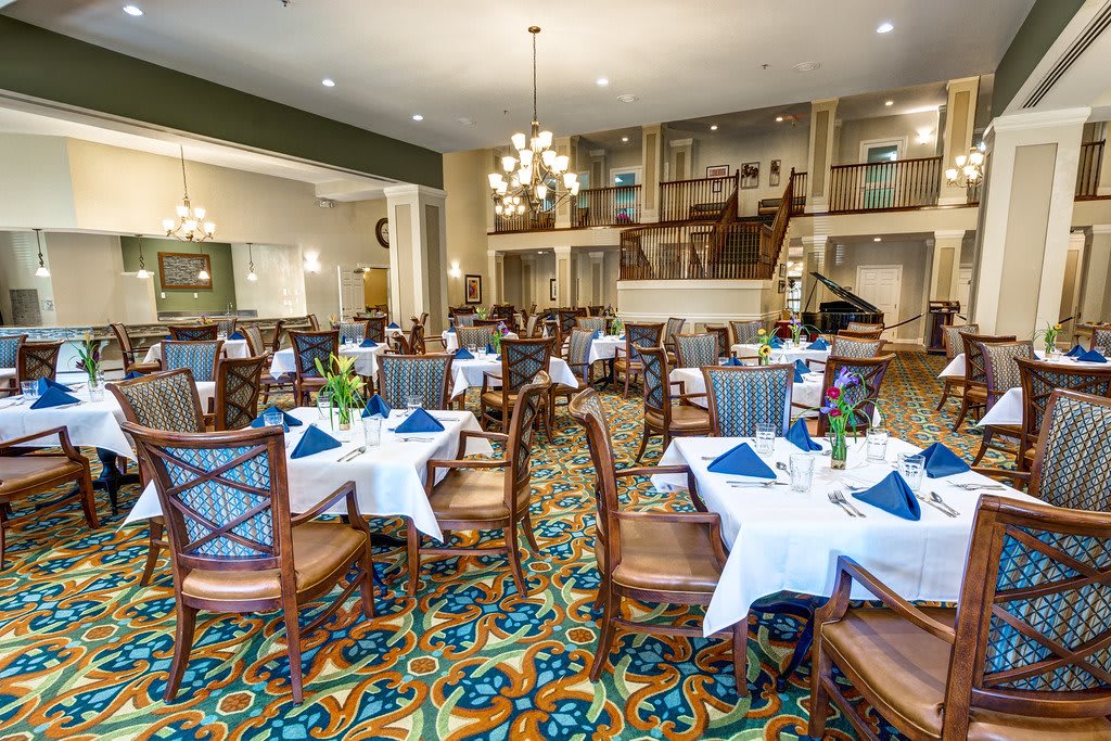 Elegant dining room with neatly arranged tables and chairs, featuring chandeliers and a patterned carpet.