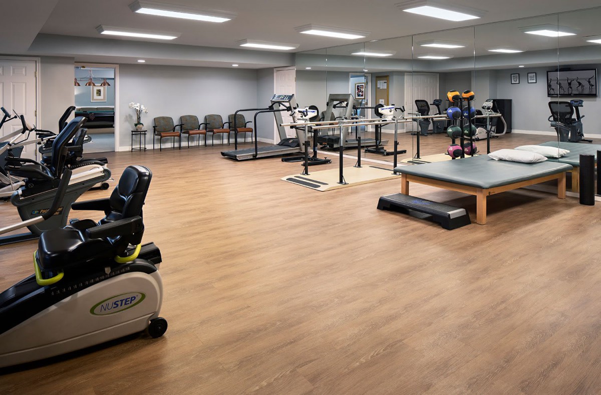 A well-equipped indoor gym with various exercise machines and wooden flooring.