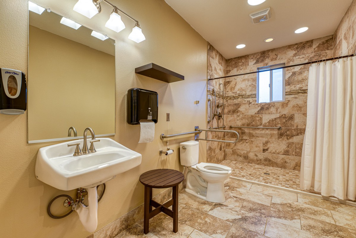 A modern, accessible bathroom with tiled walls, featuring a sink, toilet, and walk-in shower with grab bars.