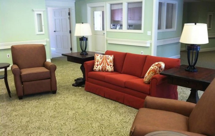 A cozy living room with a red sofa, armchairs, and a lamp on a side table.