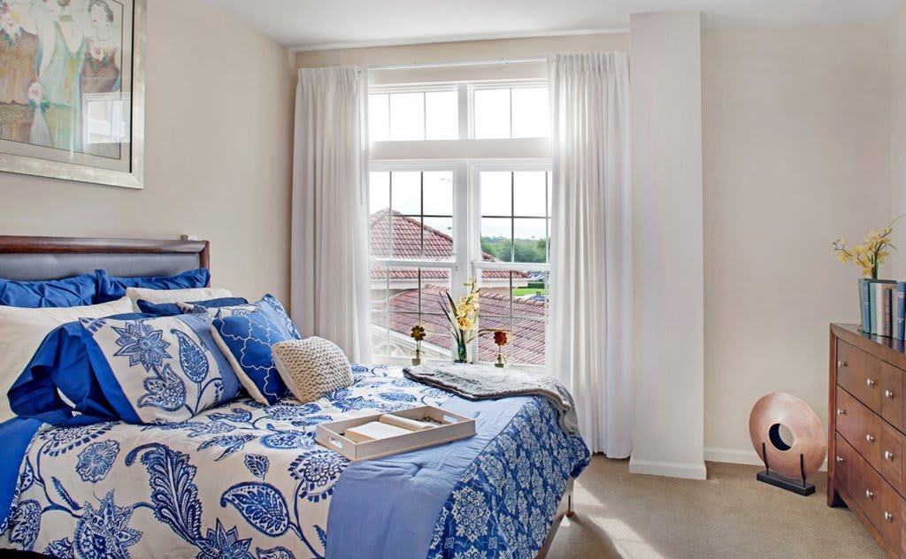 A cozy bedroom with blue and white decor, featuring a large window that lets in ample natural light.