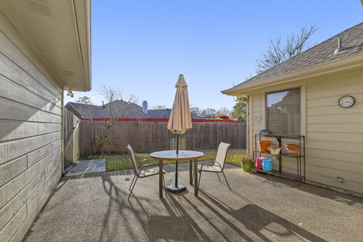 A sunny backyard patio with a table and chairs under an umbrella.