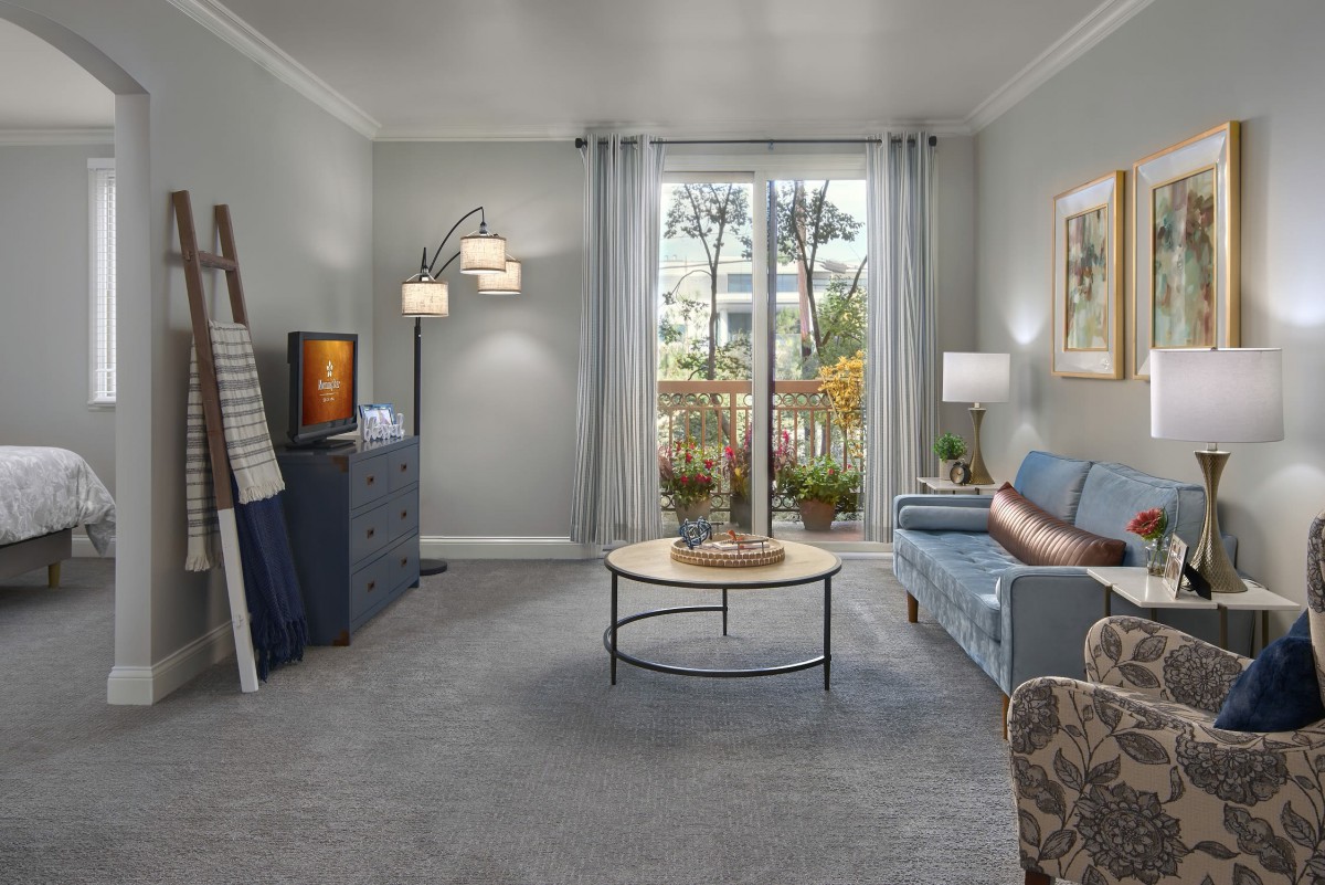 A modern living room with a cozy sofa, stylish lamp, and a coffee table in front of large windows.
