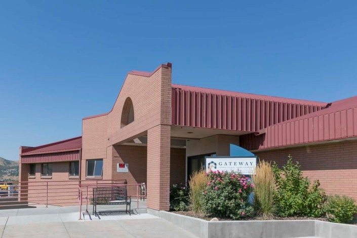 A brick building with a red roof and entrance, featuring signage and outdoor landscaping.