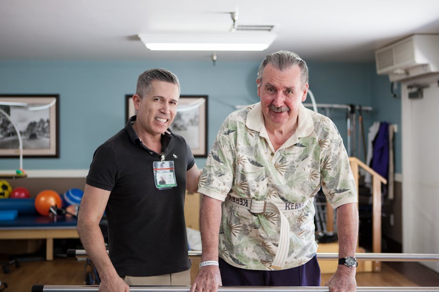 A healthcare professional assists an elderly man during a physical therapy session.