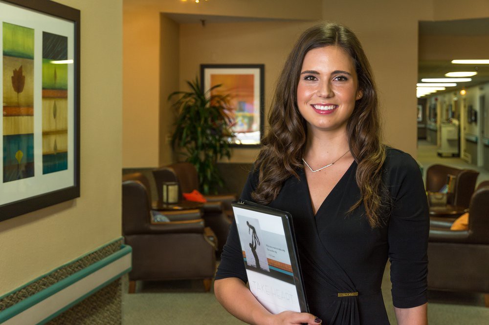 A professional woman smiling in an office environment, holding a folder.