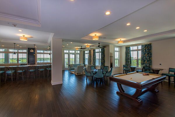 A spacious and modern living area featuring a pool table, elegant furnishings, and ample natural light streaming through large windows.