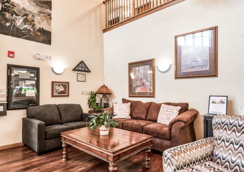 A cozy living room with a high ceiling, featuring two sofas, a wooden coffee table, decorative plants, and framed artwork.
