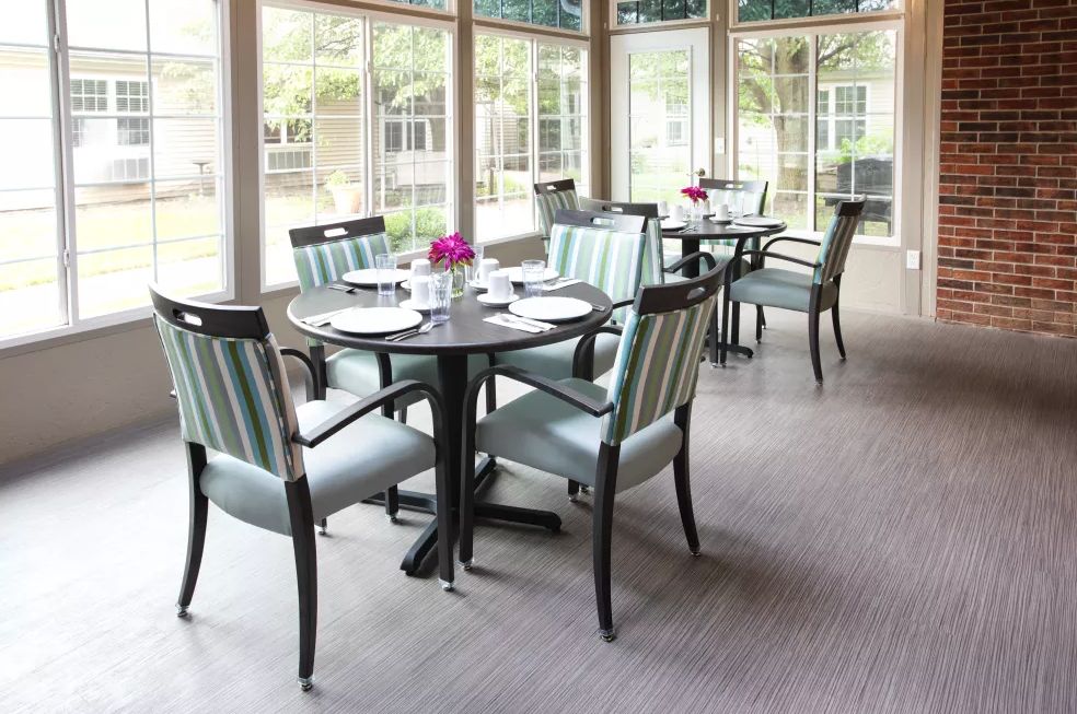 A bright and modern dining room with neatly arranged tables and chairs, surrounded by large windows.