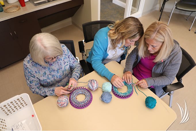 A group of women sitting together at a table, engaged in a knitting project with colorful yarn.