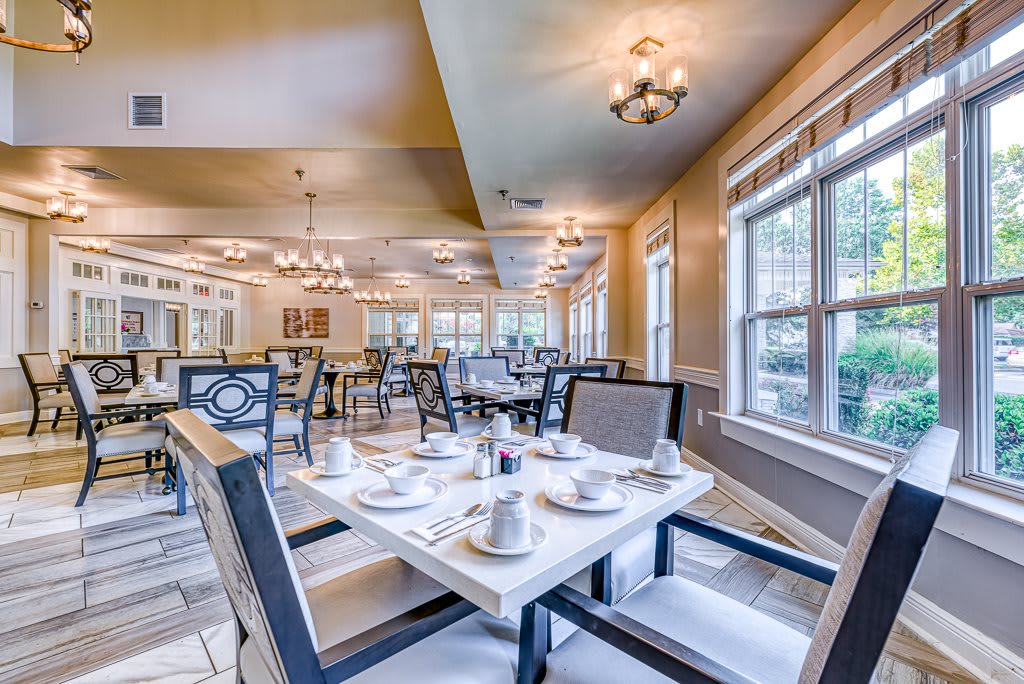 An elegant dining room with neatly arranged tables and chairs, featuring large windows and warm lighting.
