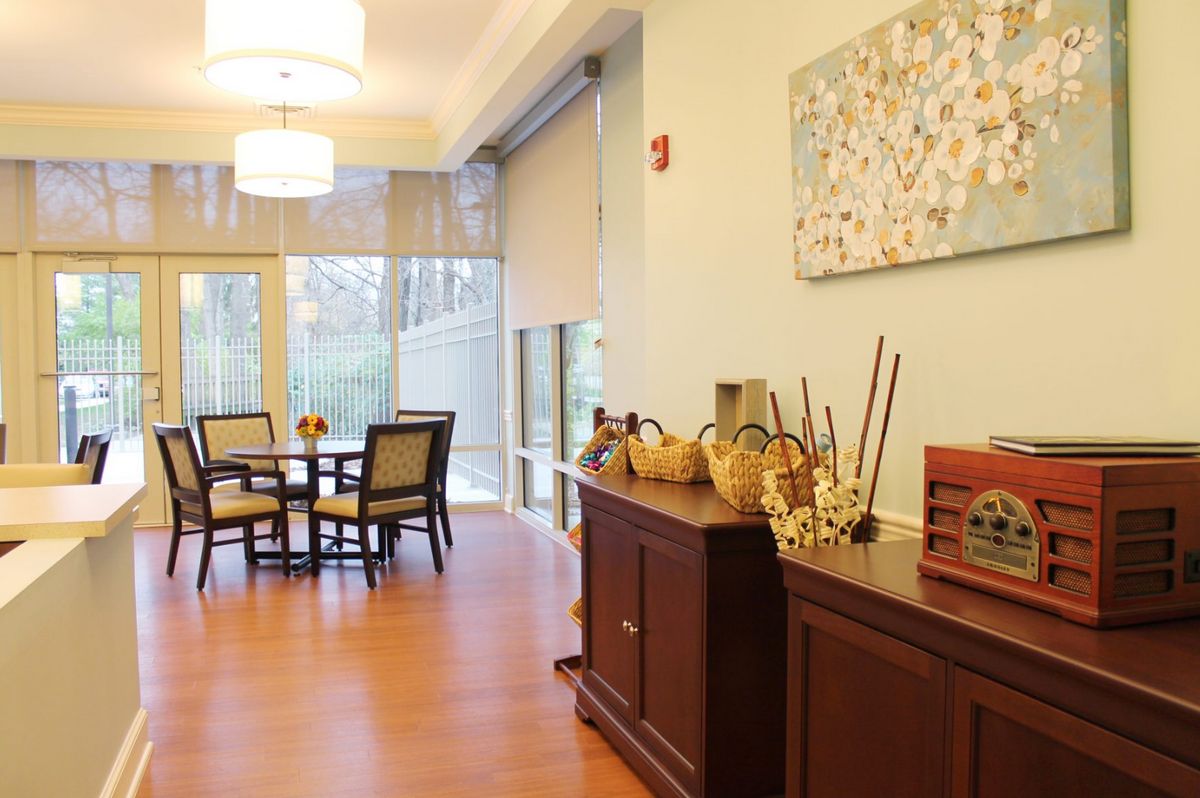 A well-lit dining room with a table and chairs, featuring large windows and decorative elements on a sideboard.
