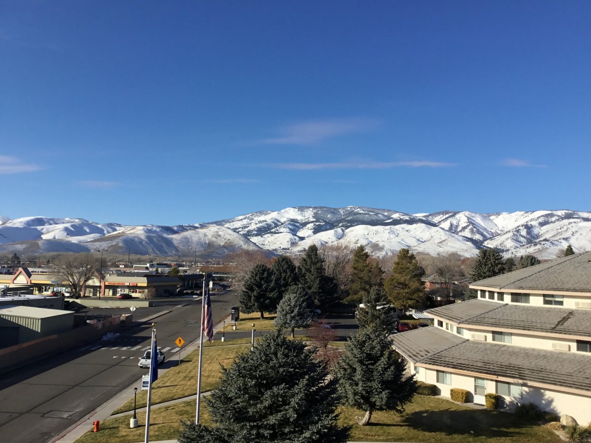 A scenic view of snow-capped mountains behind a residential area under a clear blue sky.