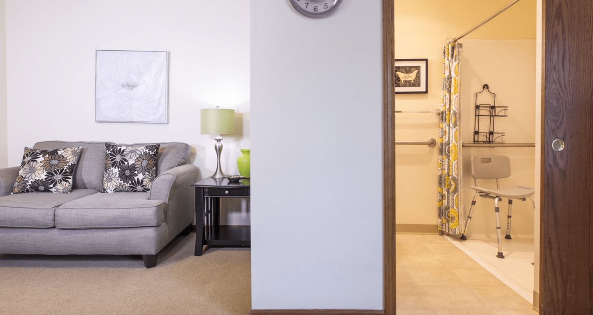 A cozy living room with a sofa, lamp, and wall clock, featuring a view into an adjacent room.