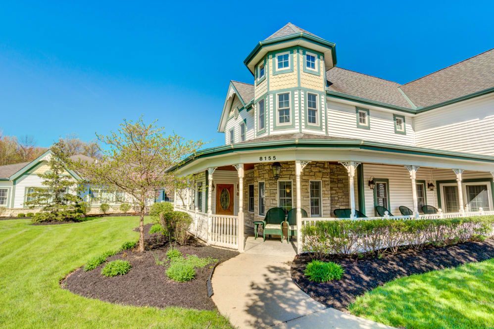 A charming Victorian-style house with a wraparound porch and well-maintained garden on a sunny day.