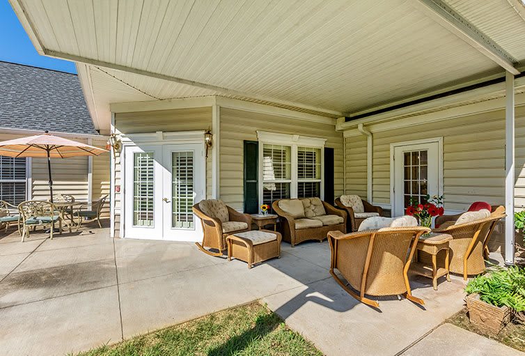 A cozy patio with wicker chairs and a sofa under a covered porch, accessed through French doors on a sunny day.