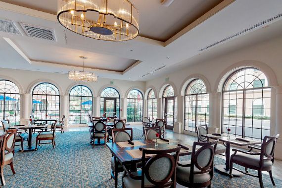 A luxurious dining room with elegant chandeliers, large windows, and neatly arranged tables and chairs.