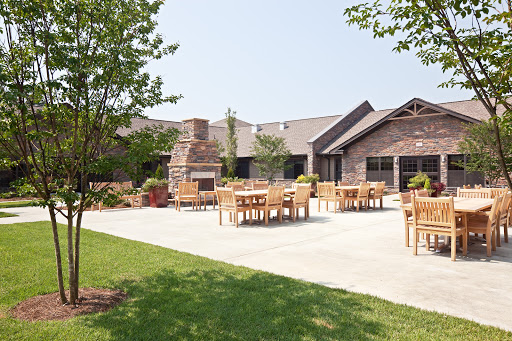 A sunny outdoor patio area with tables and chairs, surrounded by well-maintained grass and landscaping.
