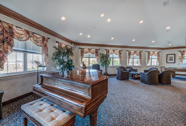 A spacious and elegantly furnished living room with a grand piano, comfortable seating, and large windows allowing natural light.
