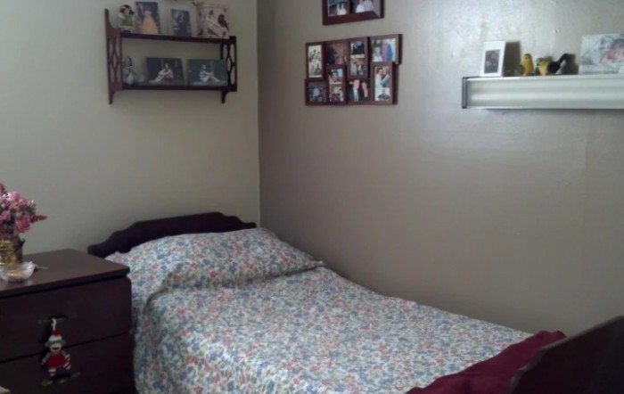 A cozy bedroom with a neatly made bed, decorated with framed photos and a small shelf.