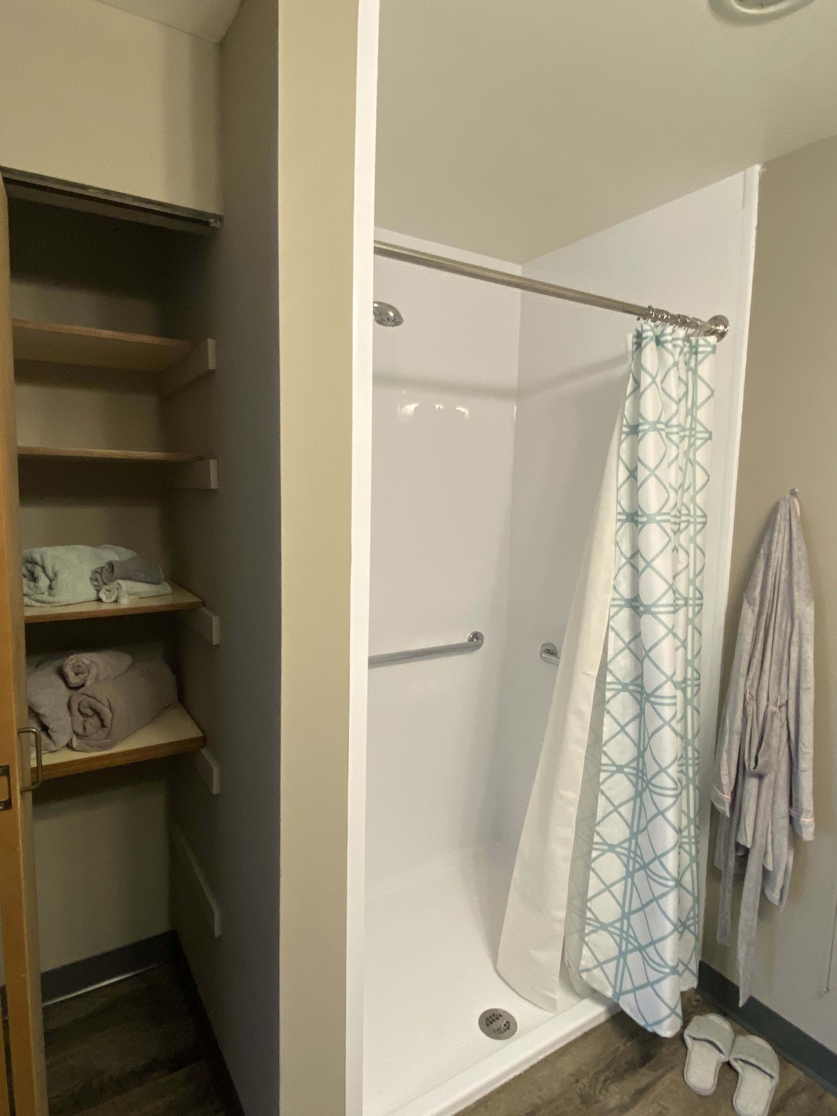 A bathroom with a shower, patterned curtain, and an adjacent shelf stocked with towels.