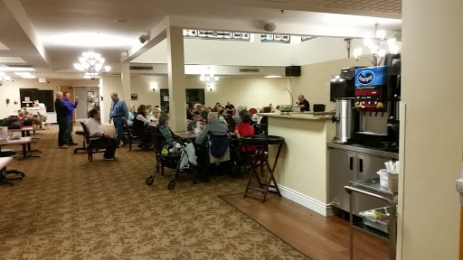 A cozy community gathering in a dining area, with people seated around tables enjoying refreshments.