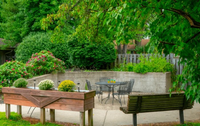 A serene garden patio with a table, chairs, and lush greenery.