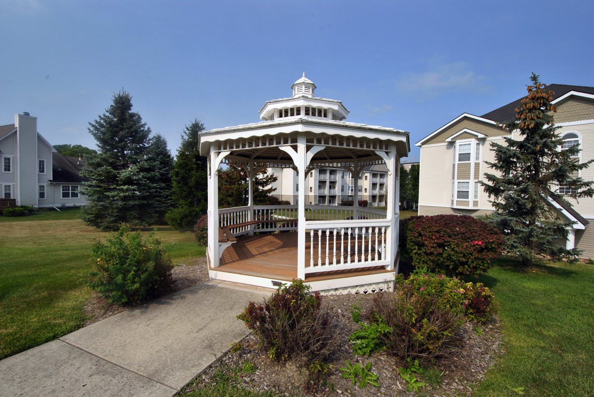 A charming gazebo situated in a garden area with surrounding greenery and a house nearby.