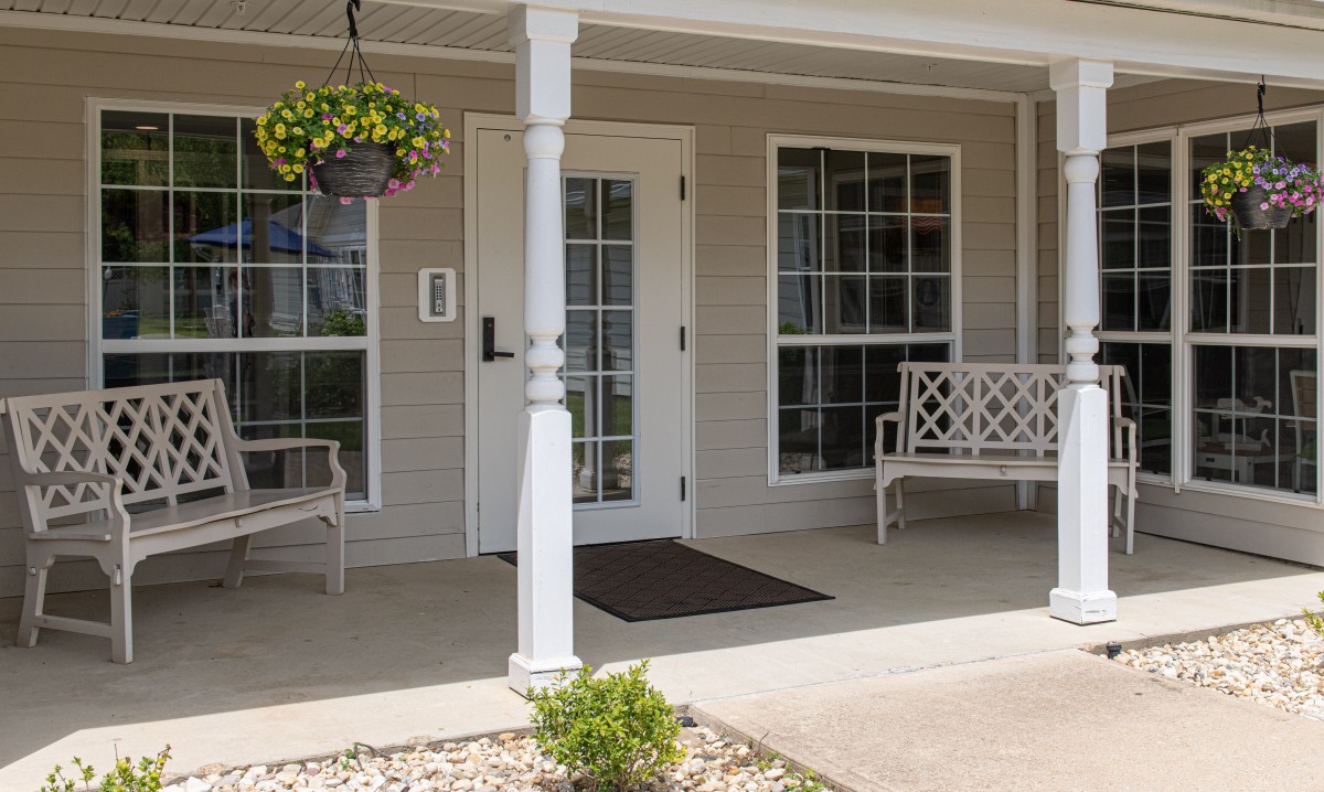 A cozy porch with benches, a hanging plant, and a welcoming entrance.