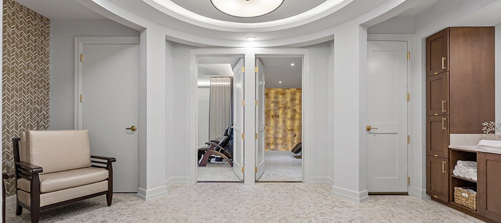 A modern interior space featuring two open doors, revealing a glimpse of chairs and warm lighting inside.