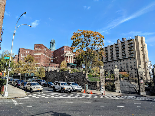A view of a historic building with an iconic statue, surrounded by trees and vehicles under a clear blue sky.