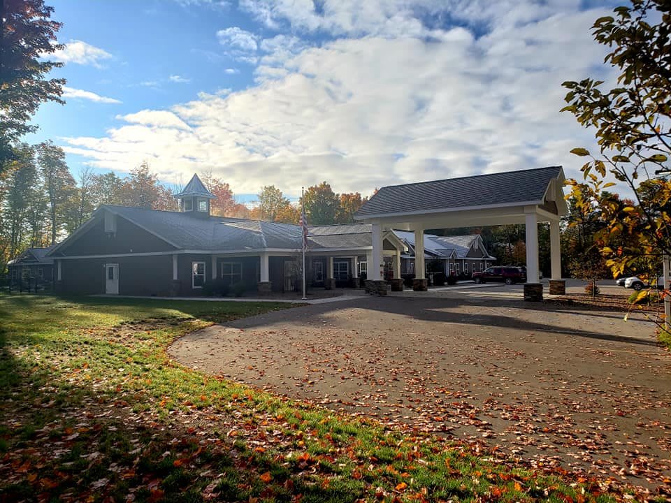 A building with a covered entrance surrounded by autumn trees and a cloudy sky.