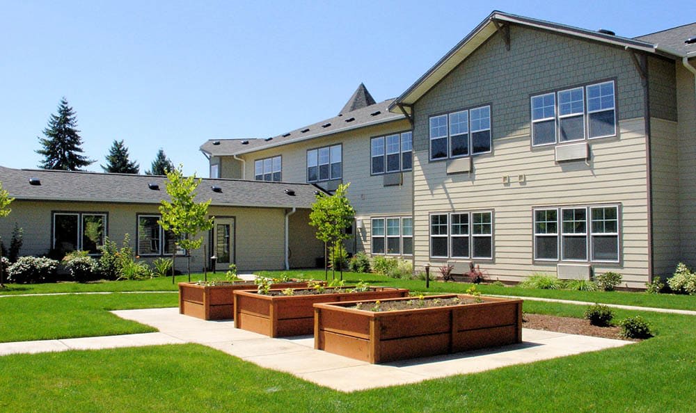 A residential building with raised garden beds and a lawn on a sunny day.