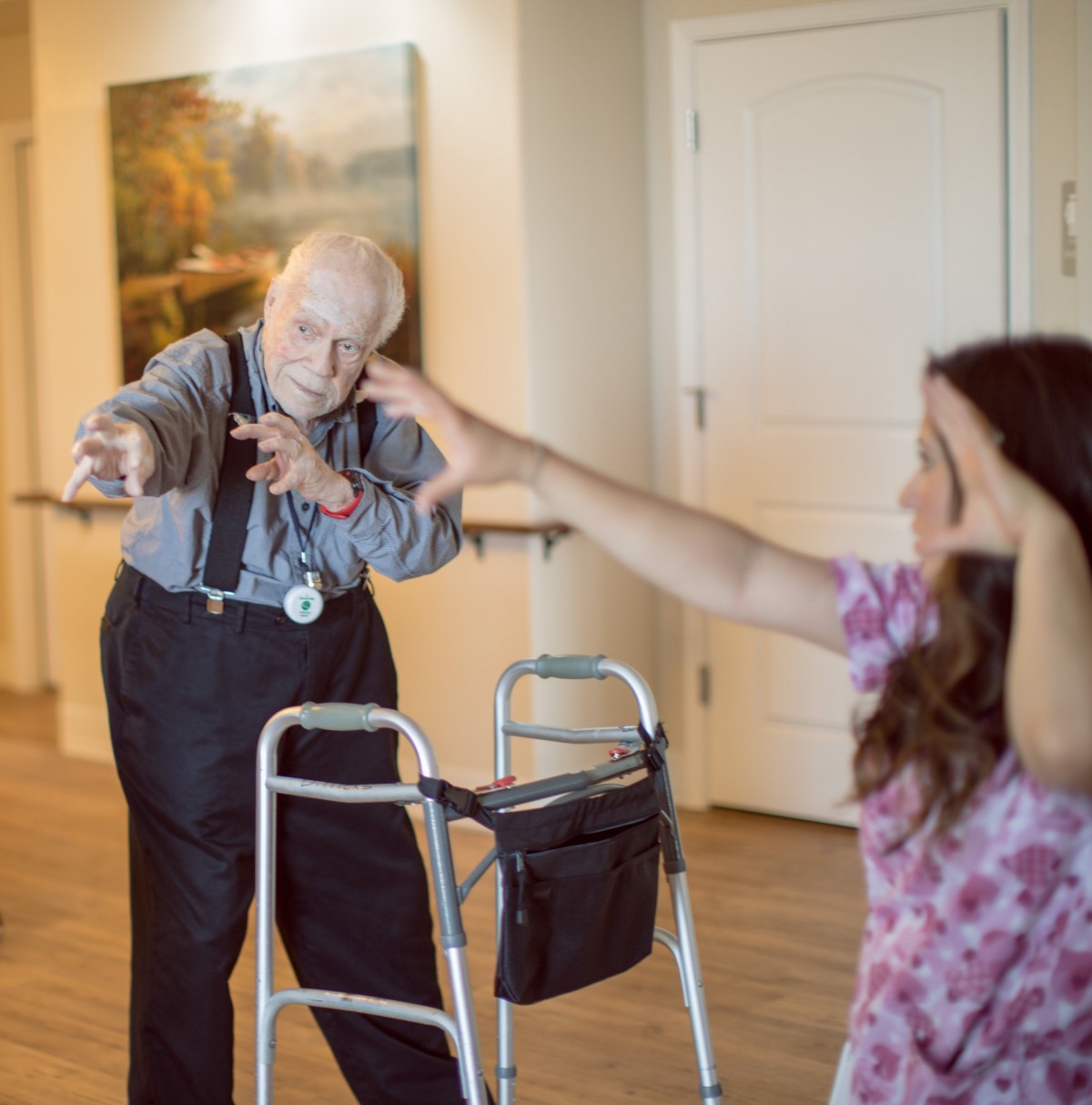 An elderly person engages in exercise with assistance from a caregiver indoors.