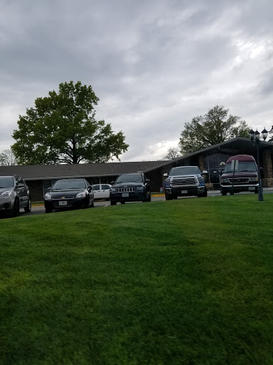 A lineup of vehicles parked on a grassy area near a building under cloudy skies.
