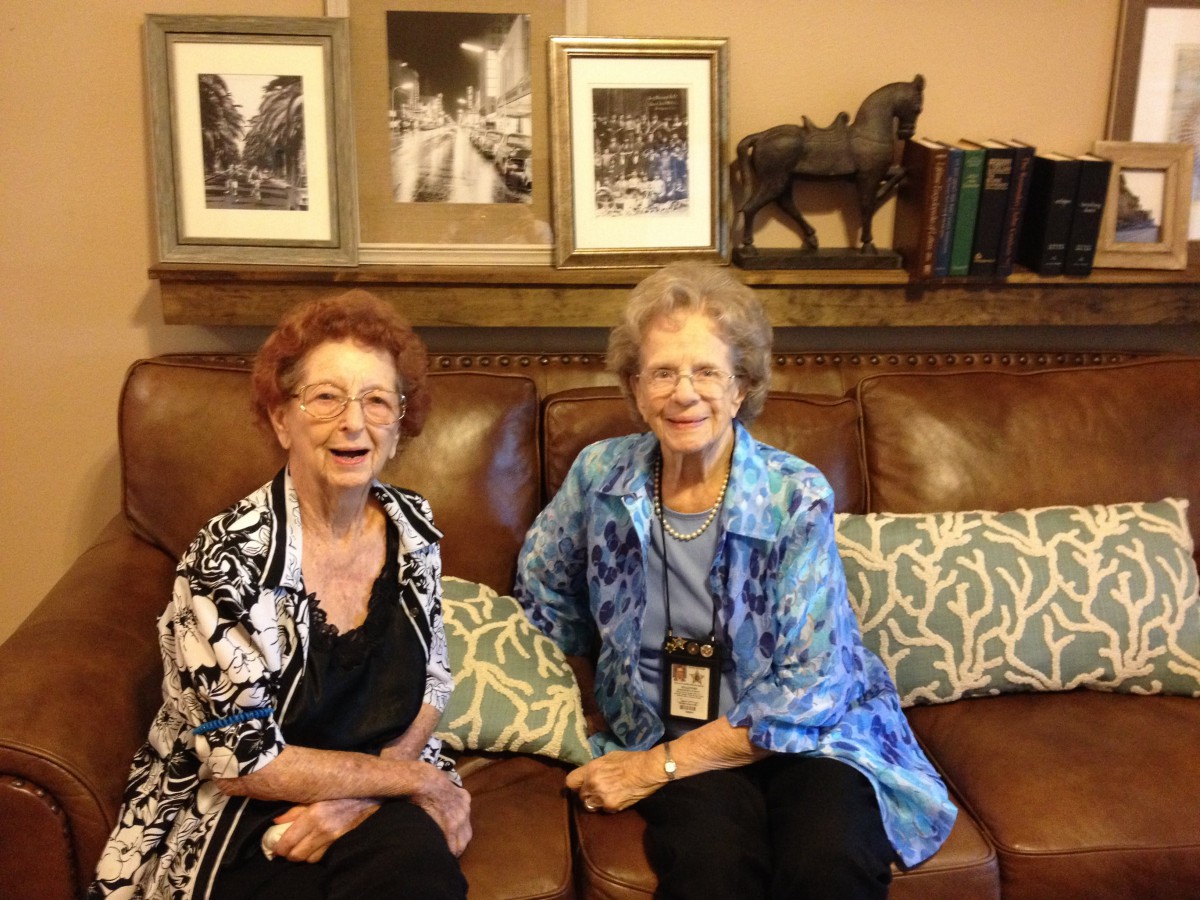 Two women sitting on a couch, smiling in a warmly decorated room.